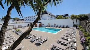 Ein Poolbereich mit Liegestühlen, einem Schwimmbecken und einem weißen Gebäude im Hintergrund.