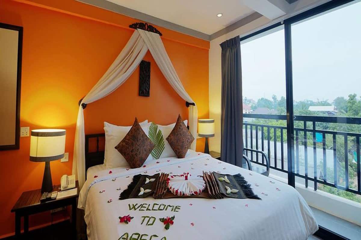 A hotel room with a bed, a nightstand, a lamp, and a view of the outdoors.