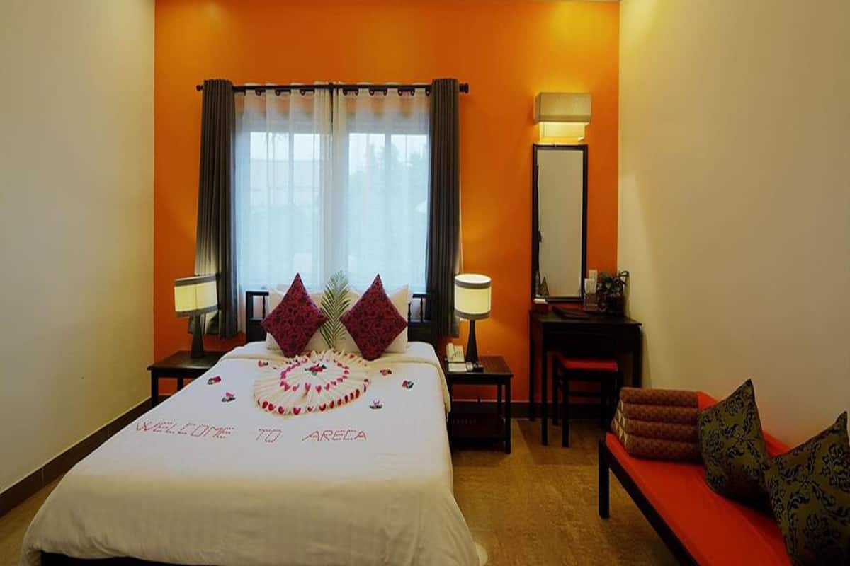 A hotel room with a bed, a desk, a chair, a lamp, and a mirror.