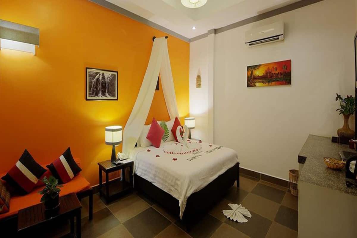 A bedroom with a bed, bedside tables, a nightstand, a chair, a desk, and a potted plant.