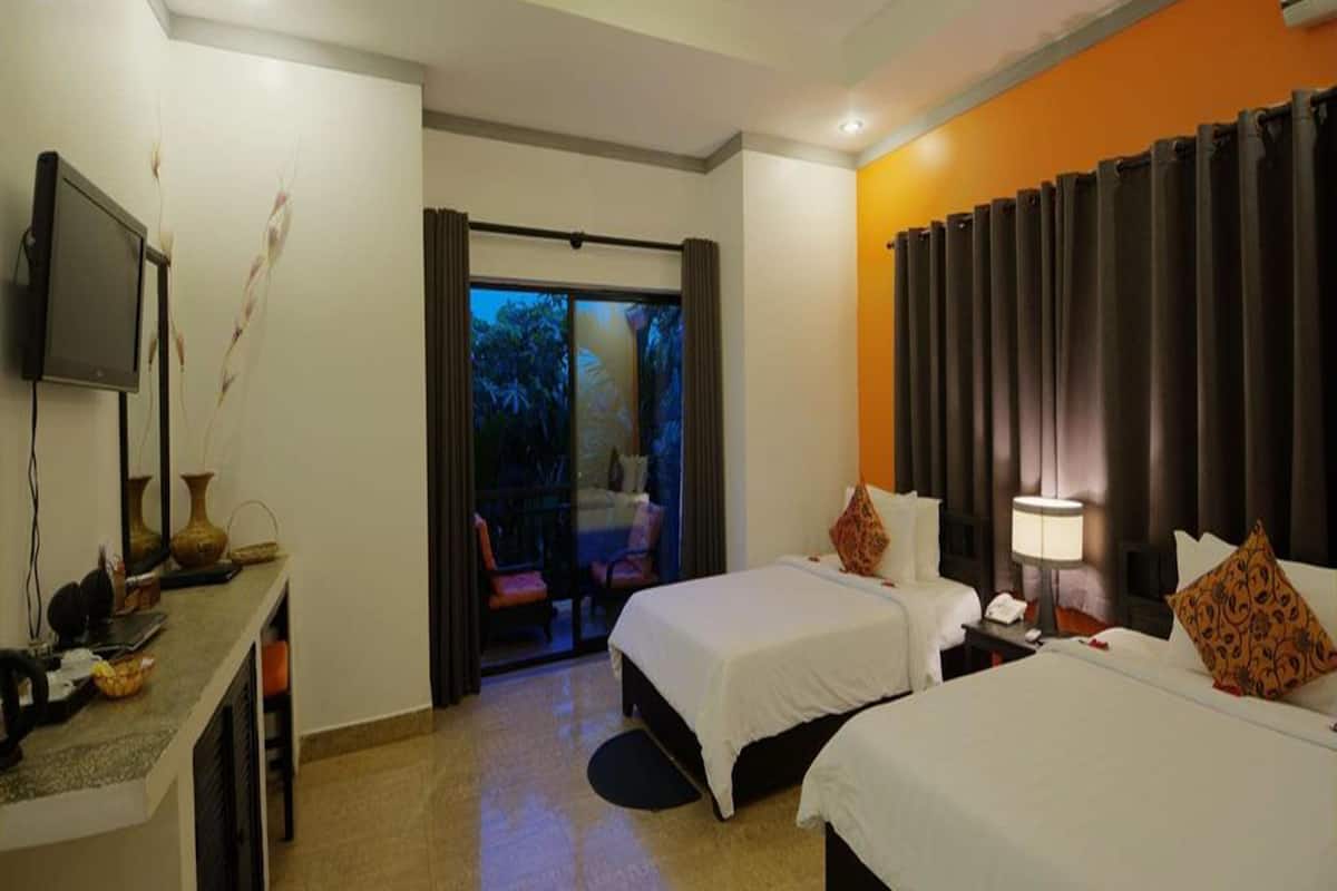 A hotel room with two beds, a desk with a television, and a sliding door to a balcony.