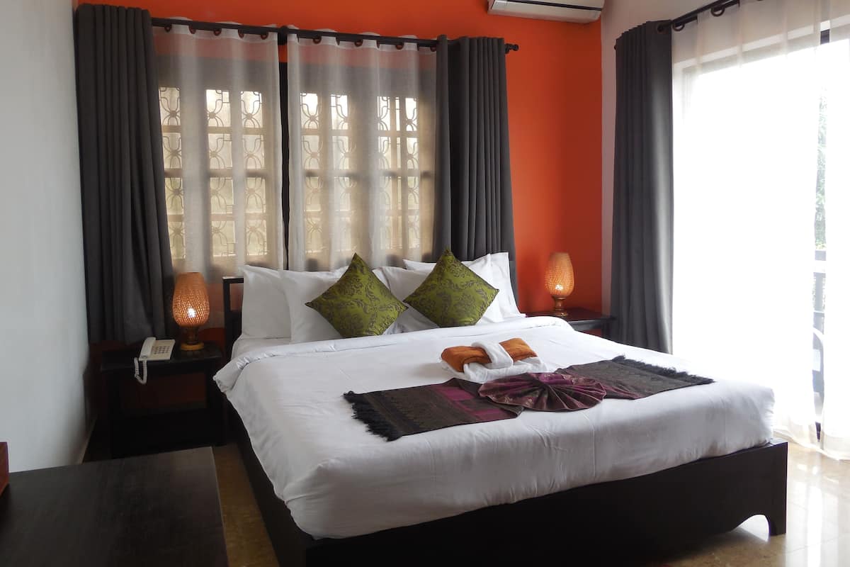 A hotel room with a large bed, two bedside lamps, a telephone, and a window with curtains.