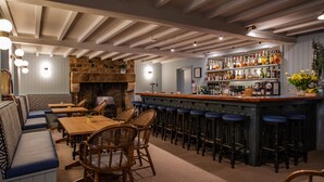 Una zona de bar con mesas y sillas de madera, una chimenea de piedra y una barra con taburetes.