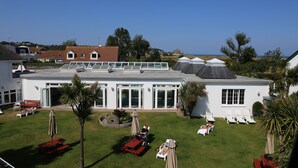 Un edificio blanco con techo plano, ventanas grandes y un patio con tumbonas y una mesa.