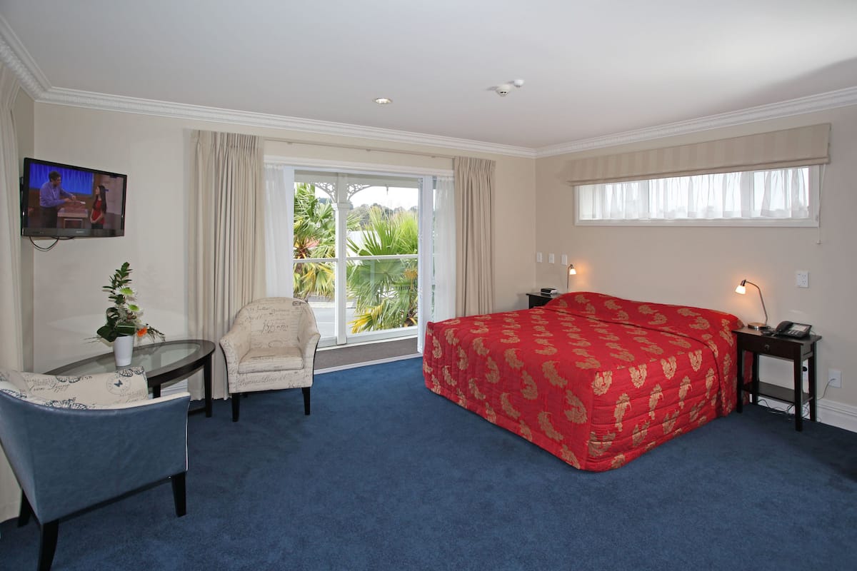 A hotel room with a large bed, a desk with a chair, a television, and a window with curtains.