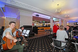 A bar area with a reception desk, chairs, and a musician playing a guitar. - Tuakau Hotel (Tuakau)