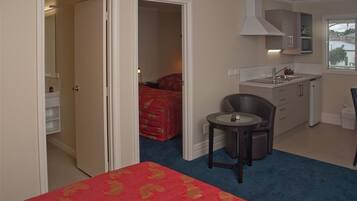 Ein Hotelzimmer mit Bett, kleinem Tisch, Stuhl, einer Küchenzeile und einem durch eine offene Tür einsehbaren Badezimmer.
