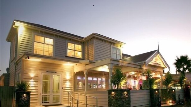 A two-story house with a covered porch, a front entrance with steps, and a small front yard with palm trees.