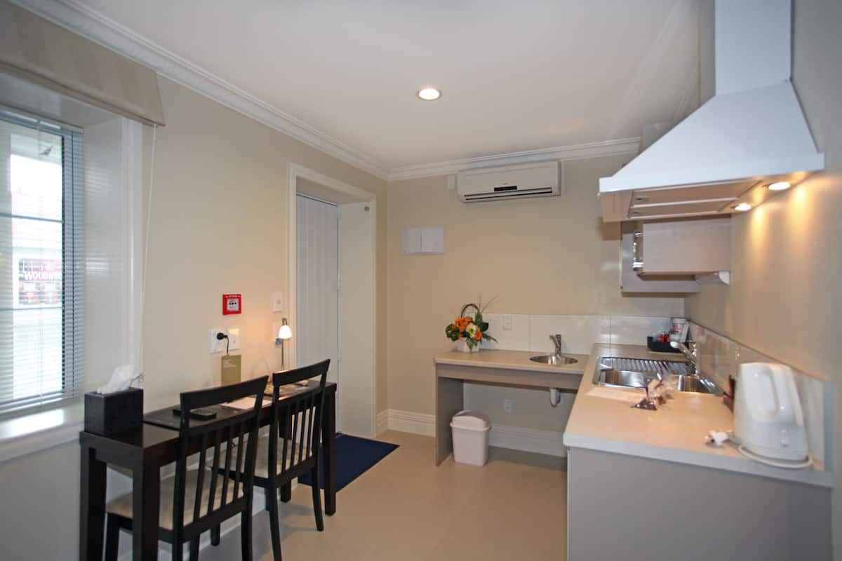 A compact kitchen with a dining area, including a table and chairs, a sink, and an air conditioning unit.