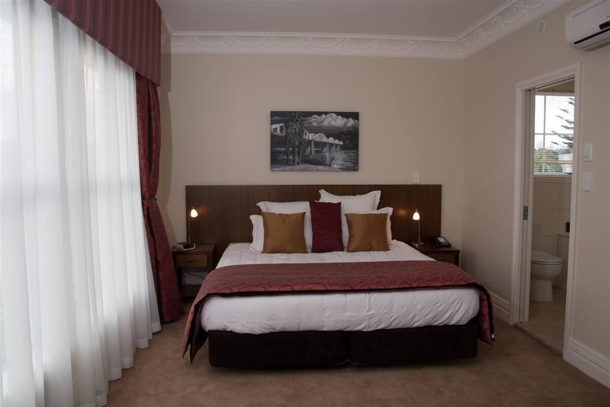 A hotel room with a large bed, a nightstand, a lamp, and a painting on the wall.