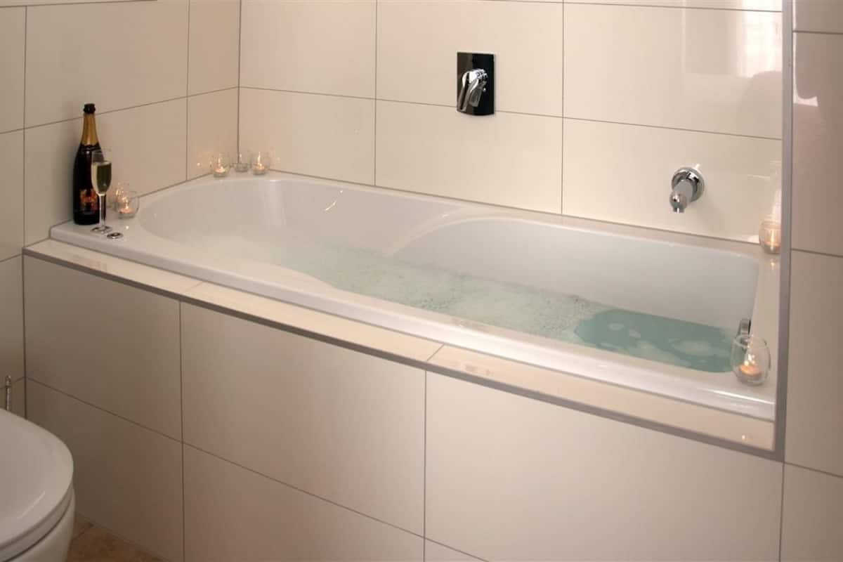 A modern bathroom with a large bathtub, a toilet, and a champagne bottle on the left.