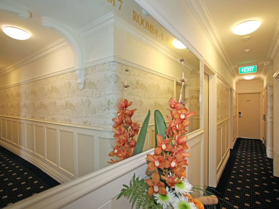 Un pasillo de hotel con piso estampado, paredes blancas y diseño de papel tapiz floral, y una señal de salida.