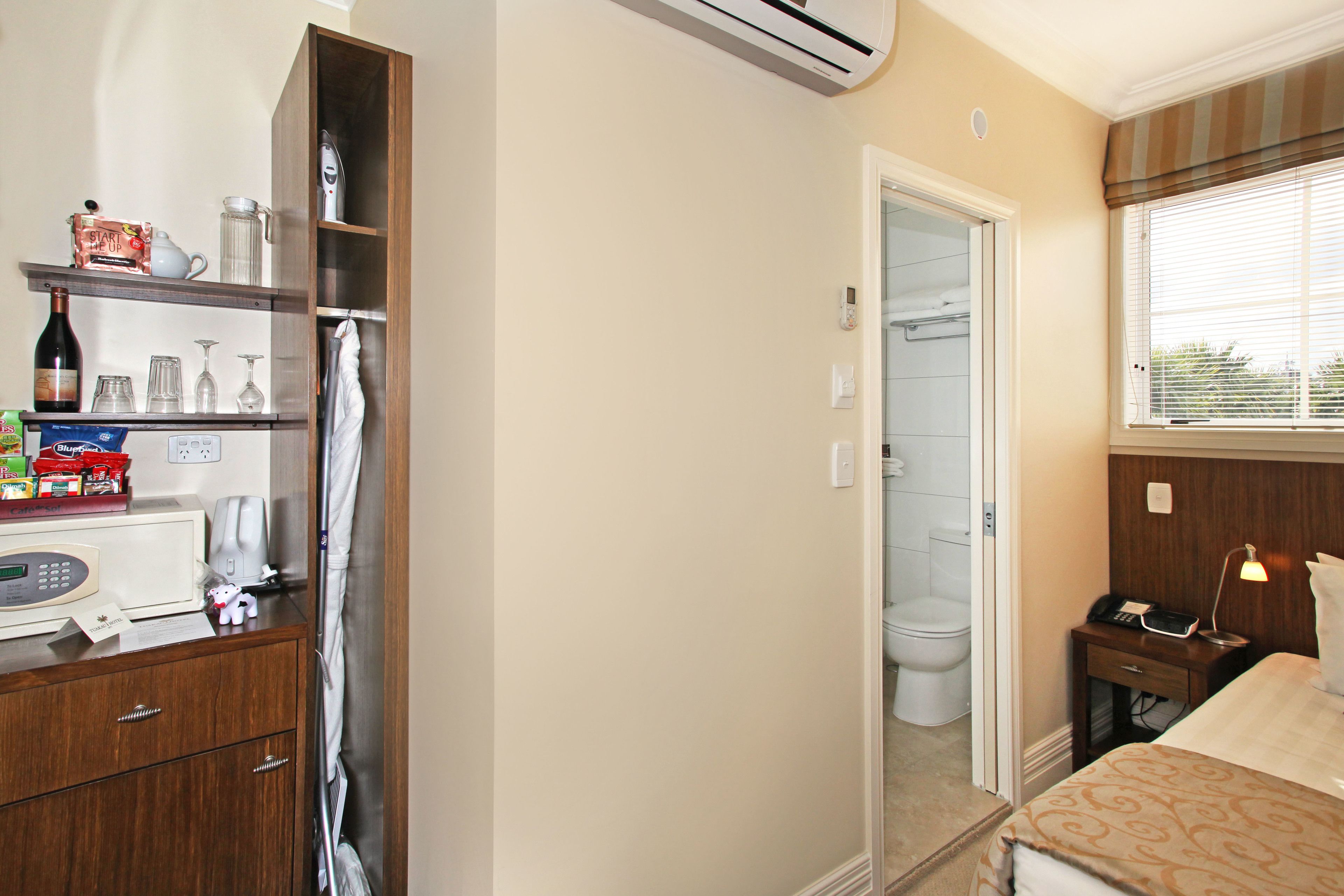 A hotel room with a wooden cabinet, a microwave, a bottle, and a bedside table with a lamp.