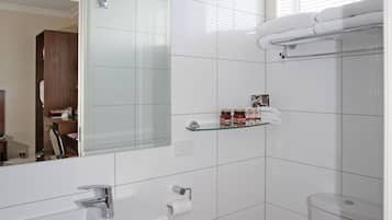 A modern bathroom with white tiles, a glass shower enclosure, a white toilet, and a vanity with a mirror and towel rack.