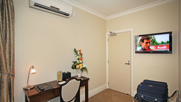 A hotel room with a desk, chair, air conditioning unit, television, and a suitcase. - Tuakau Hotel (Tuakau)