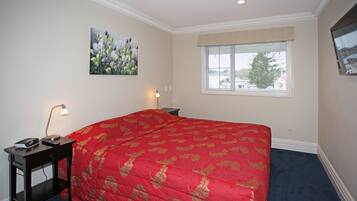 A bedroom with a large bed, a nightstand with a lamp, a painting on the wall, and a window with blinds.