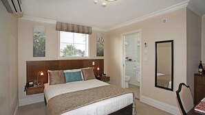 A bedroom with a large bed, bedside tables, a mirror, and a window with blinds.