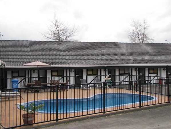 A building with a swimming pool surrounded by a fence, outdoor seating, and a covered area with tables and chairs.