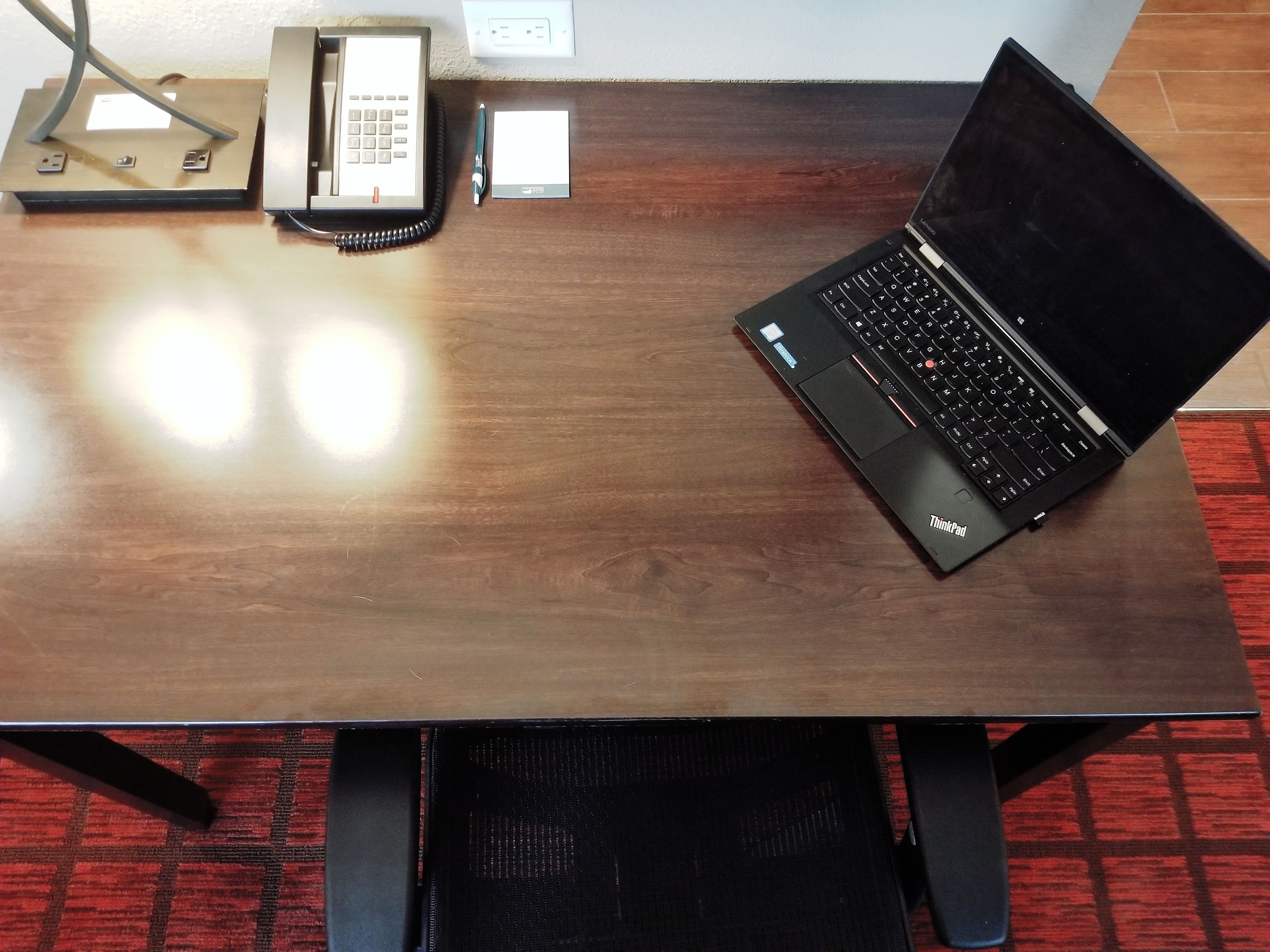 A wooden table with a laptop, a telephone, and a notepad.