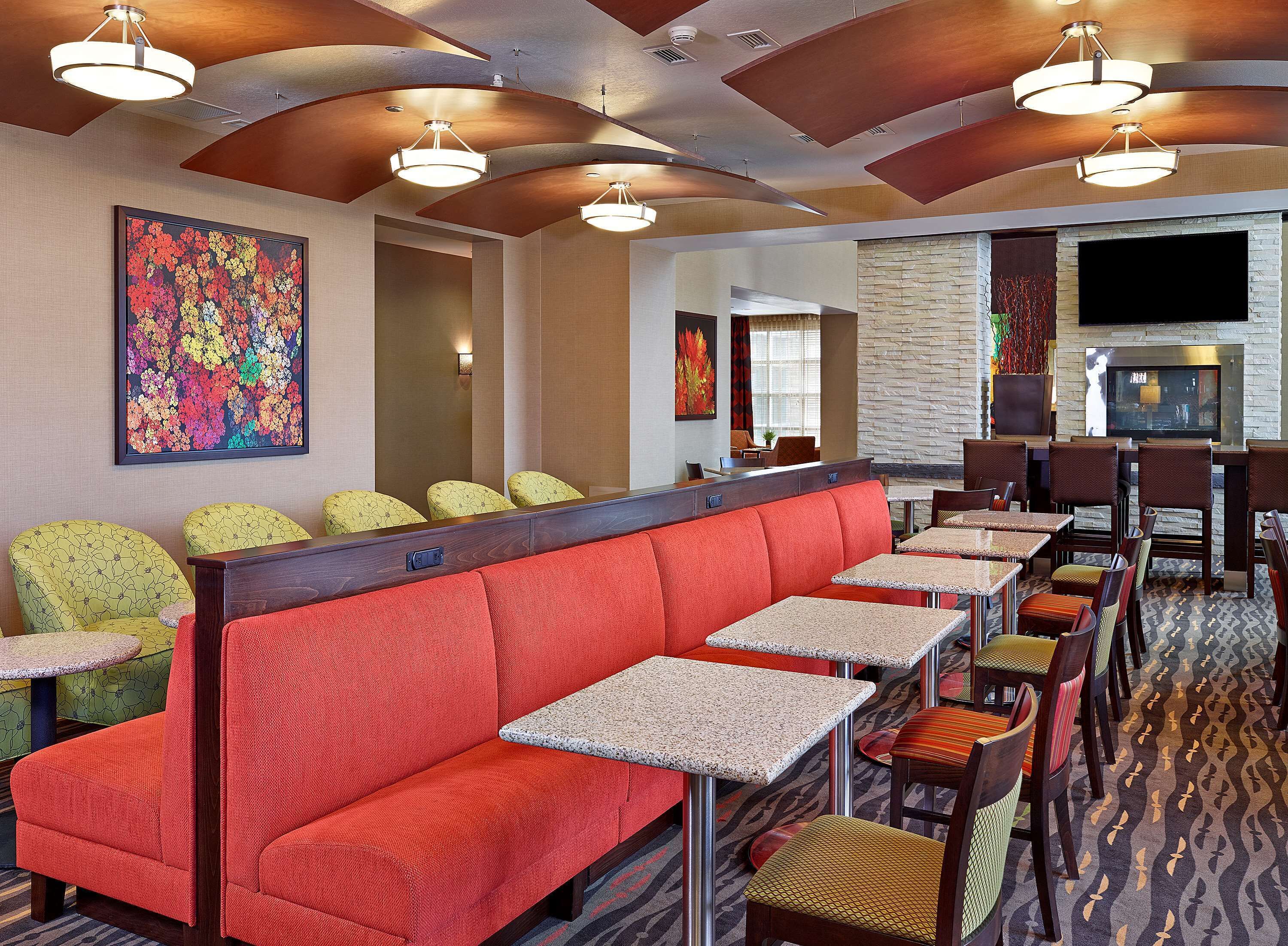 A restaurant with red booths and green chairs, a stone wall, and a TV mounted on the wall.