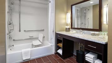 A modern bathroom with a walk-in shower, grab bars, a white bathtub, a vanity with a sink, and a large mirror.
