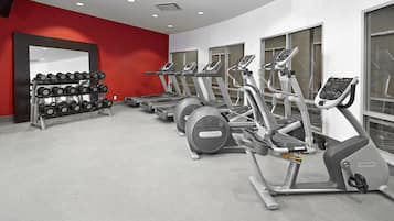 A gym with treadmills, ellipticals, and a rack of dumbbells.