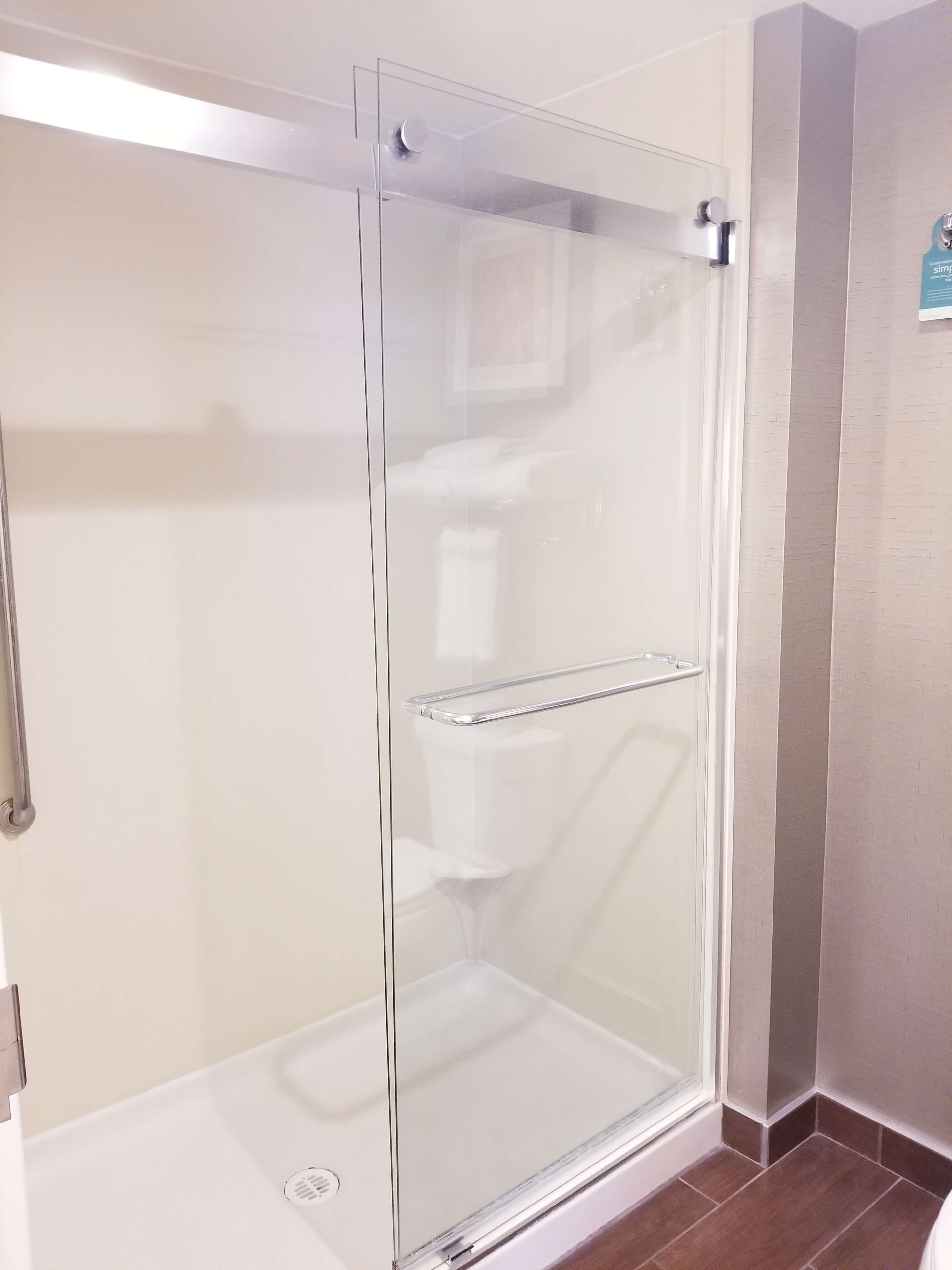 A glass-enclosed shower stall with a metal grab bar and a towel rack.