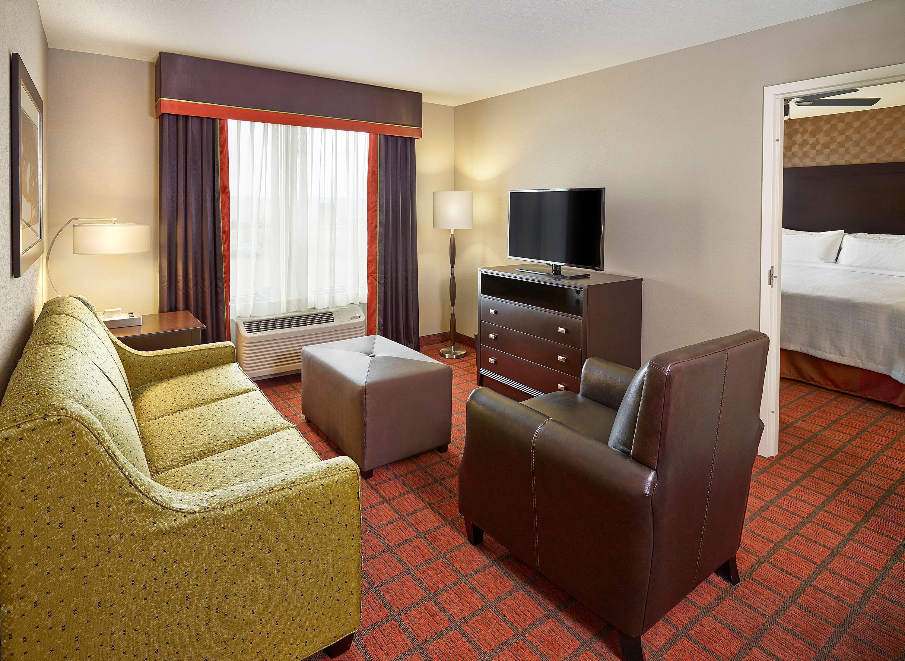 Ein Hotelzimmer mit Sofa, Ohrensessel, Hocker, Fernseher, Kommode und einem Bett.