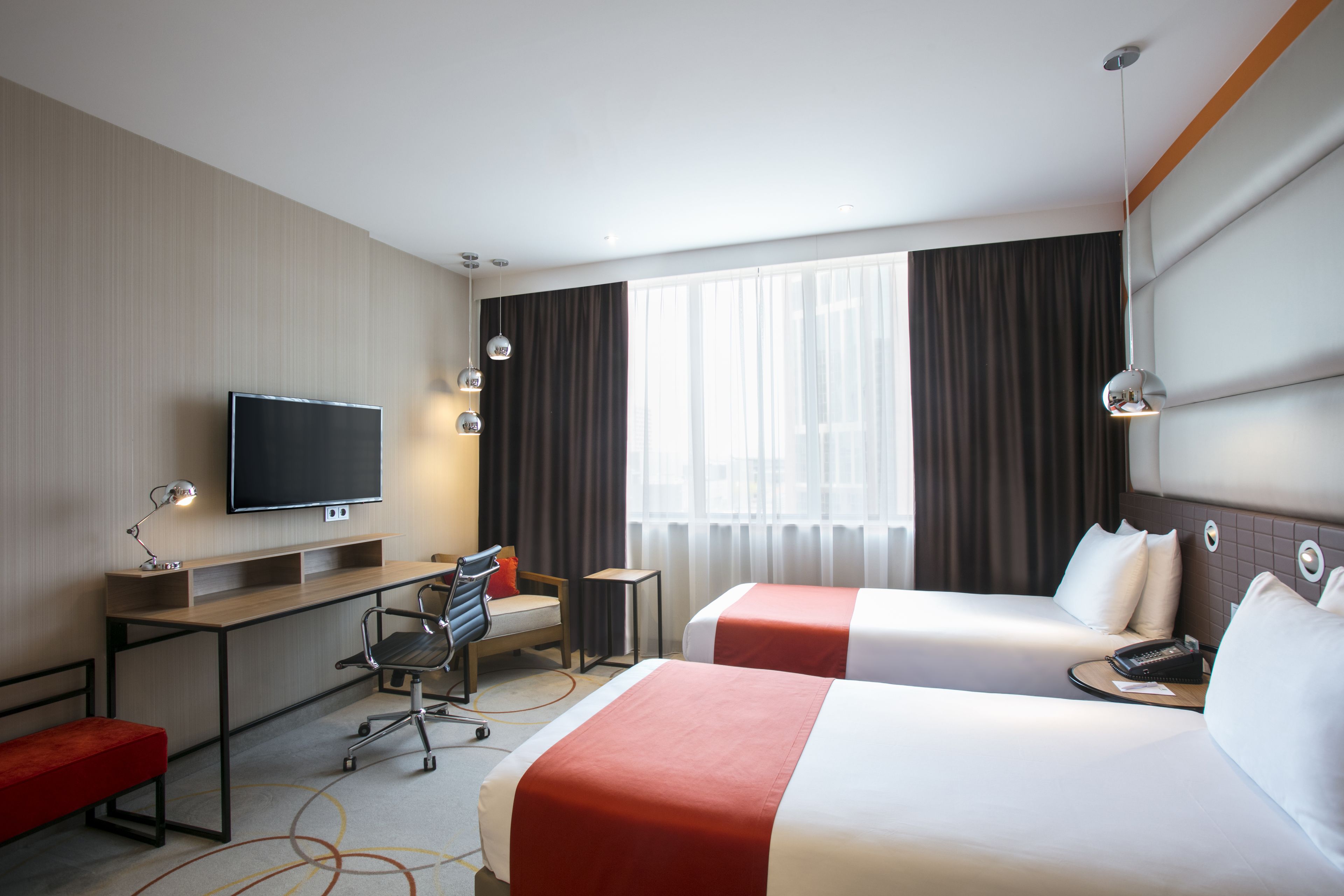 A hotel room with two beds, a desk, a chair, a TV, and a window with curtains.