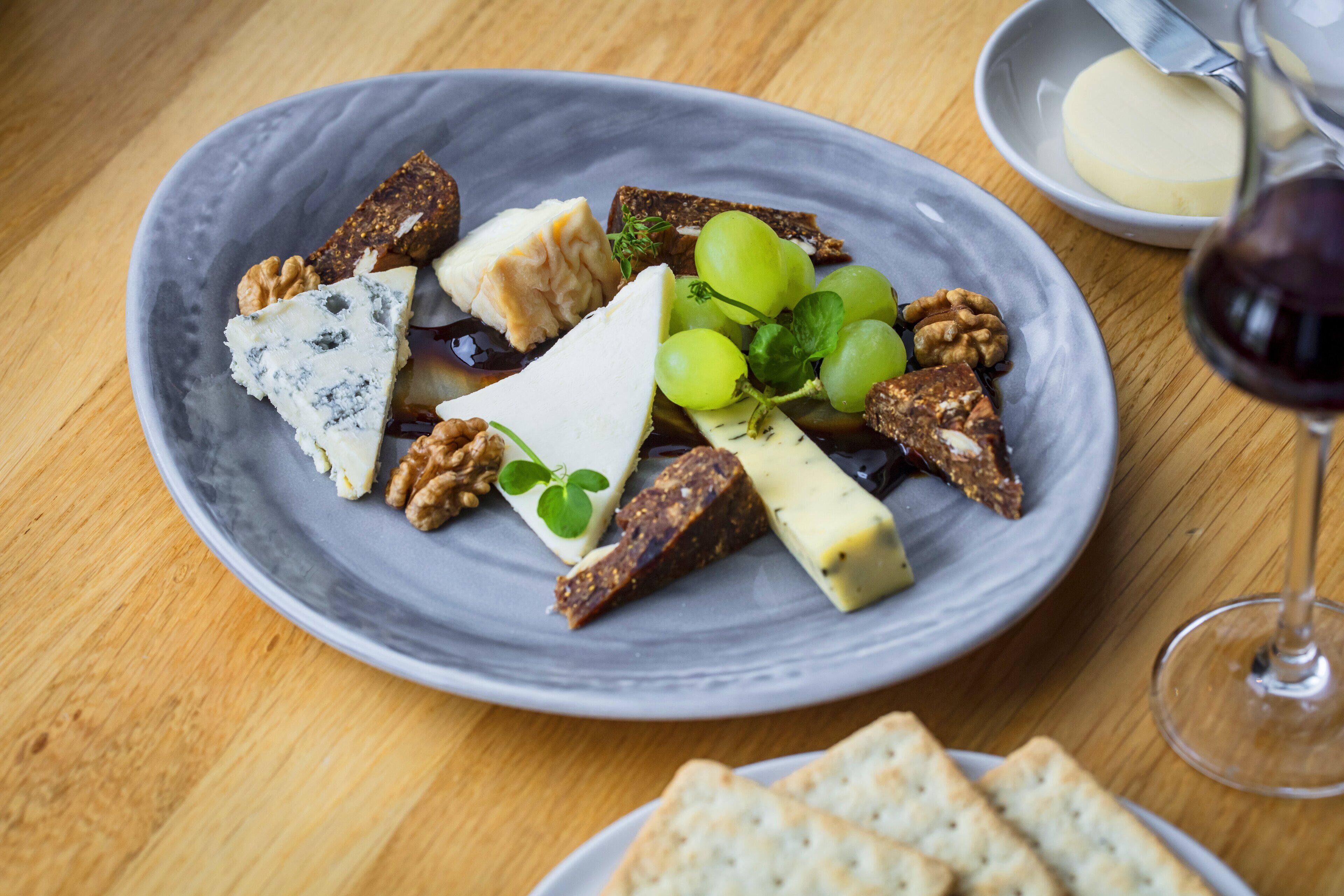Un plato de quesos variados, uvas y nueces sobre una mesa de madera.
