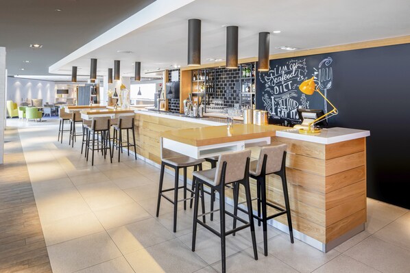 Un espace bar moderne avec des tabourets hauts, un comptoir et un mur noir où sont écrits des messages inspirants.