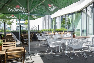 Un espace extérieur aménagé avec des tables et des chaises, dont certaines sont dotées de parasols, ainsi que des plantes en pot.