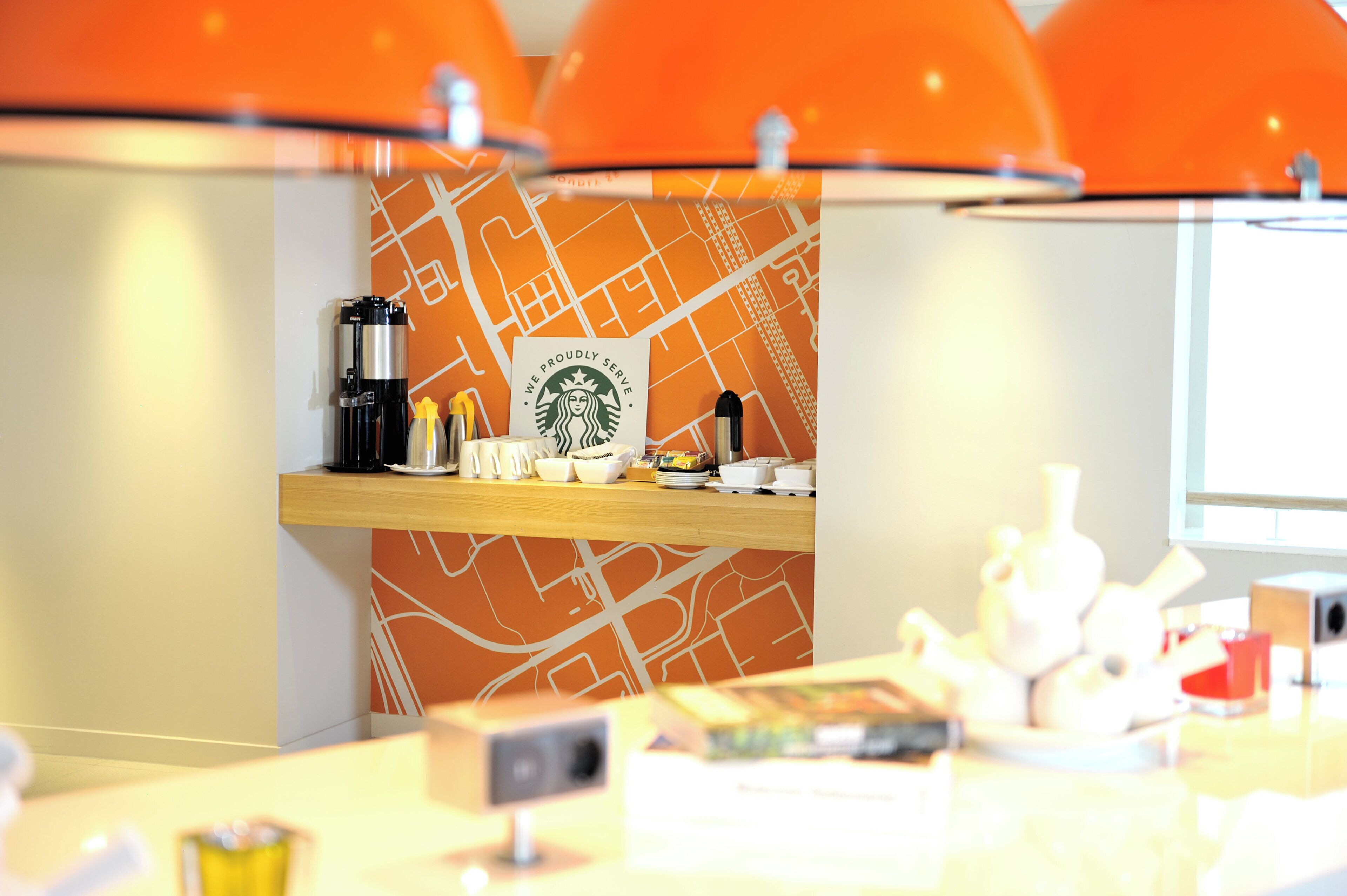 A modern interior with a wooden counter, a Starbucks sign, and orange lighting fixtures.