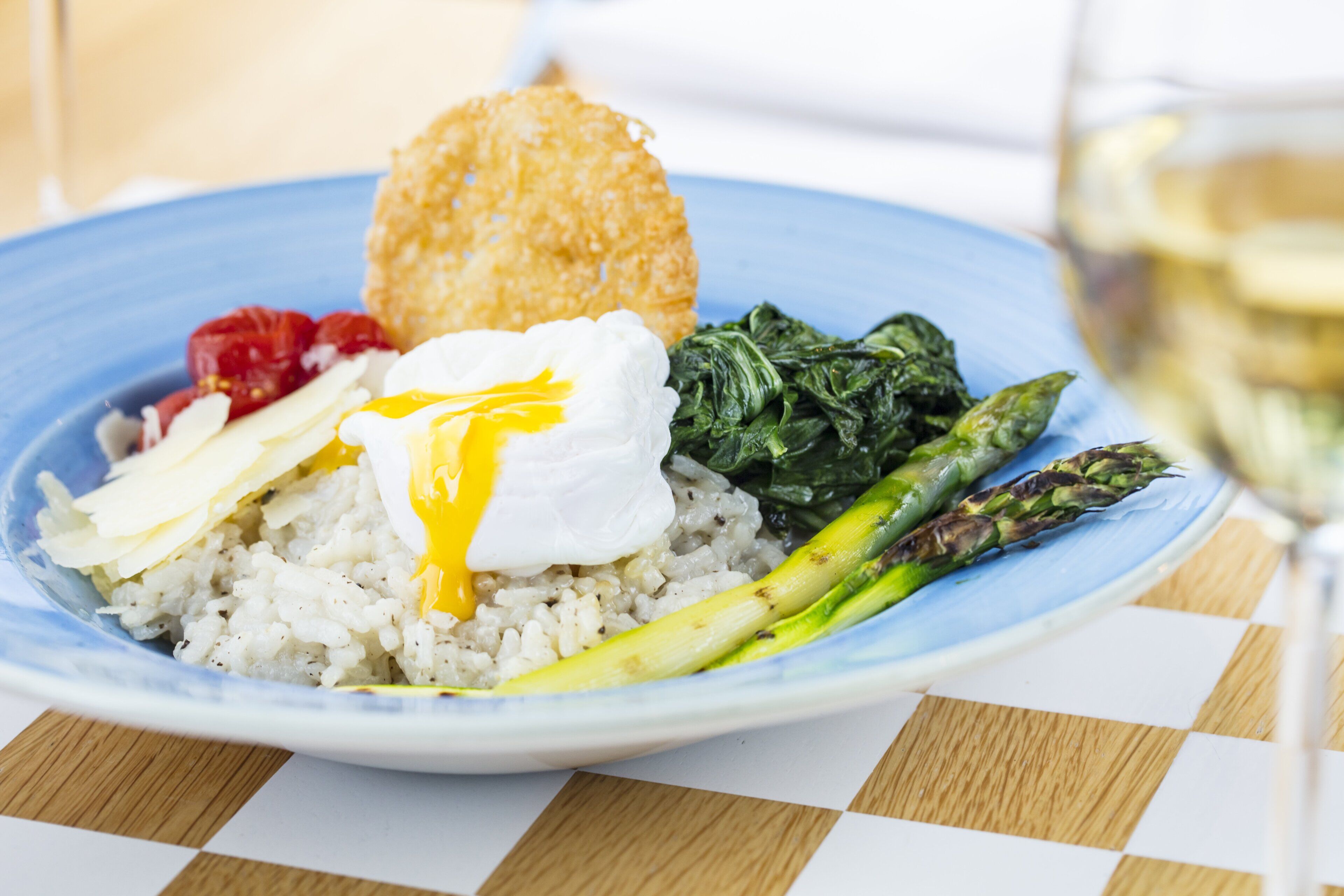 Un plato con arroz, espárragos, espinacas, un huevo pochado y un alimento frito, posiblemente una croqueta, sobre un plato azul.