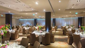 Une salle de banquet avec de nombreuses tables rondes, chacune recouverte d’une nappe blanche et agrémentée d’un arrangement floral.