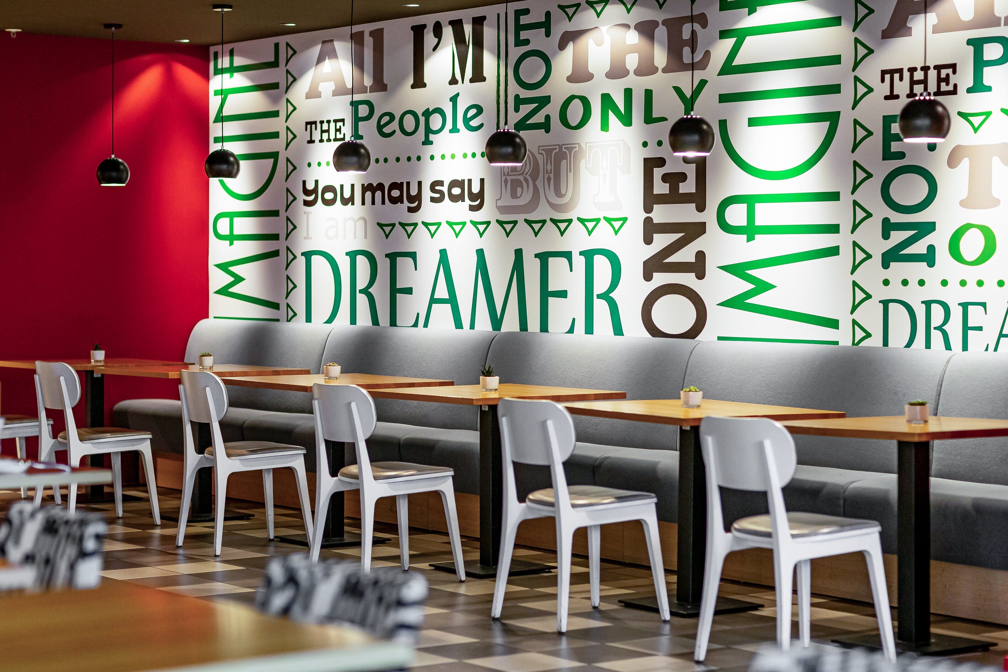 A modern cafe interior with white chairs and tables, a red accent wall, and motivational wall art.