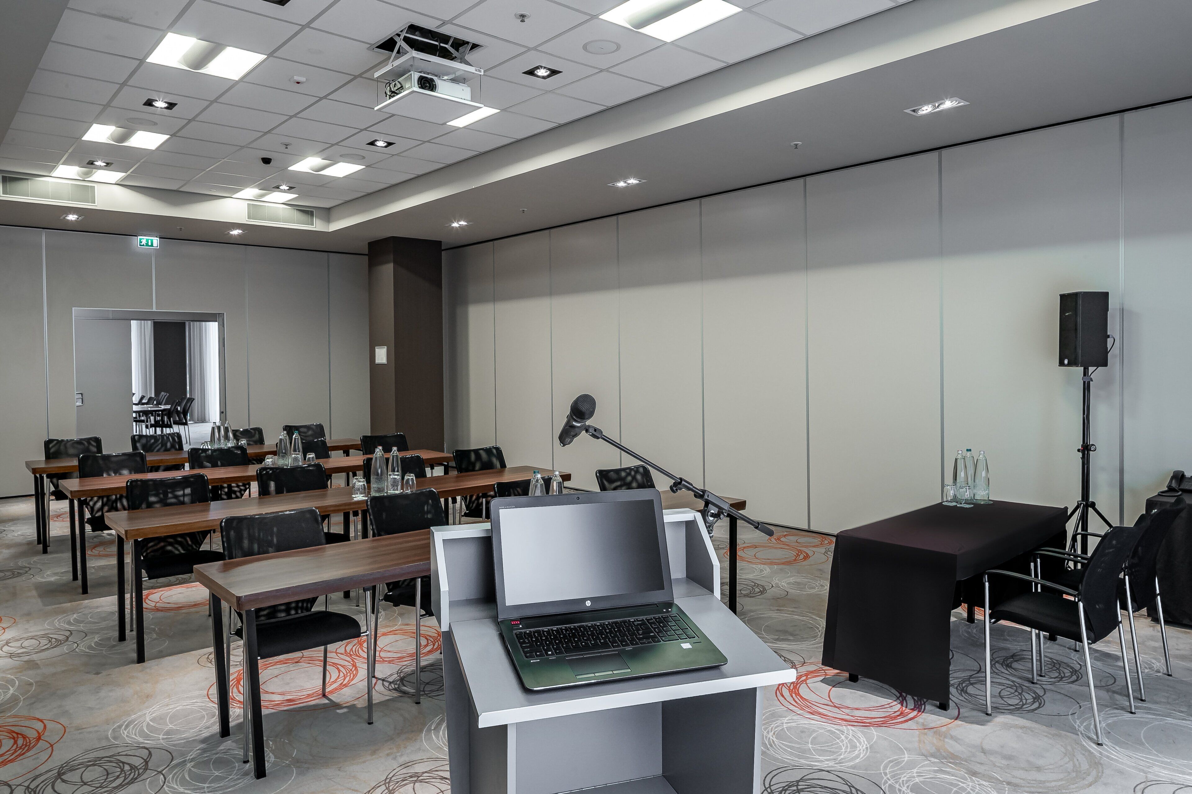 A conference room with tables, chairs, a podium, a laptop, a microphone, and a speaker.