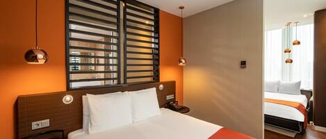 Habitación de hotel con una cama grande, mesitas de noche, un espejo y una ventana con cortinas.