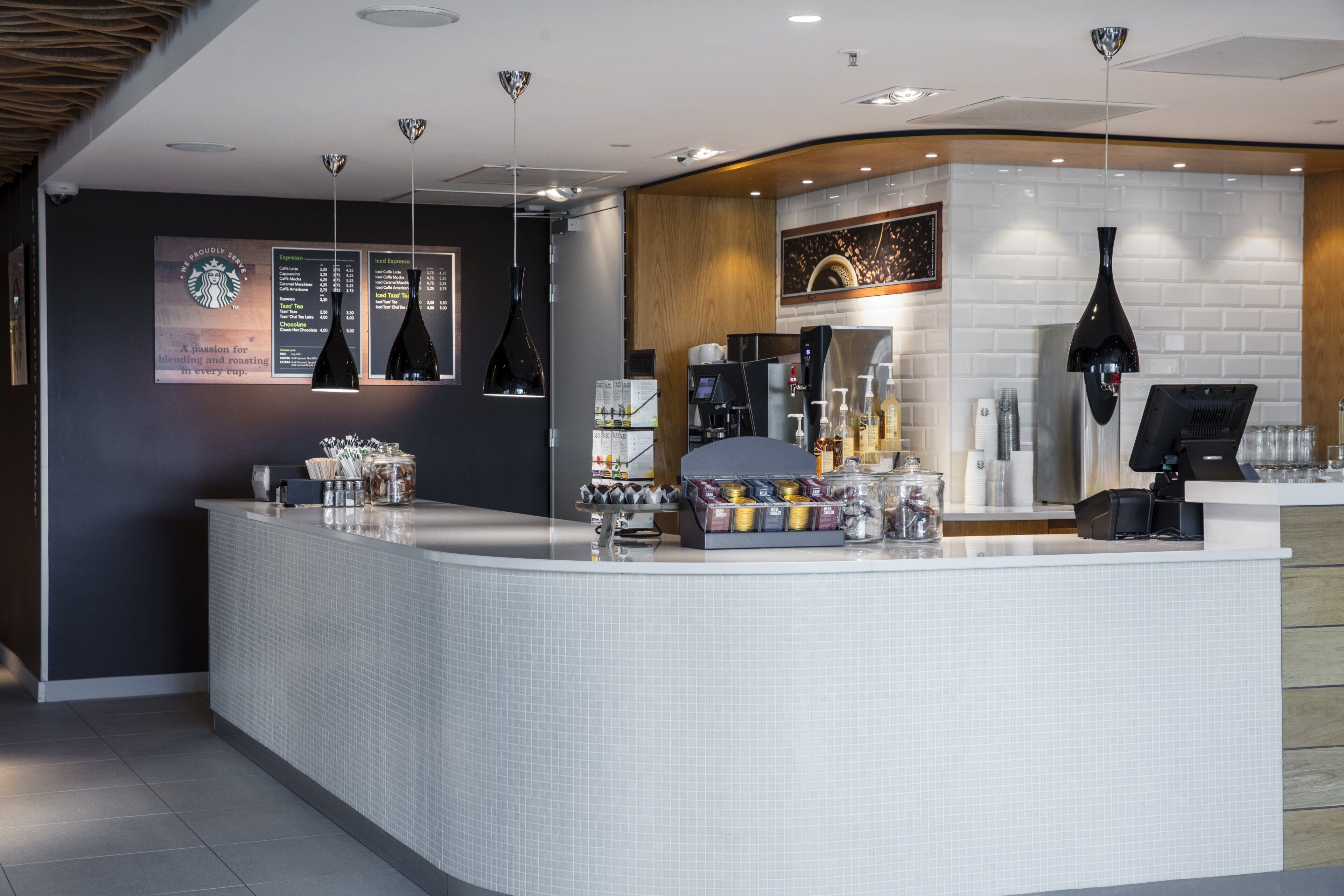 A modern bar area with a curved counter, espresso machine, and menu boards.