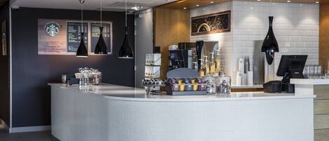 Un espace bar moderne doté d’un comptoir incurvé, d’une machine à expresso et de panneaux d’affichage pour les menus.