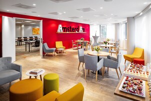 Un hall d’hôtel moderne avec un mur rouge, plusieurs espaces de détente et une table de buffet.