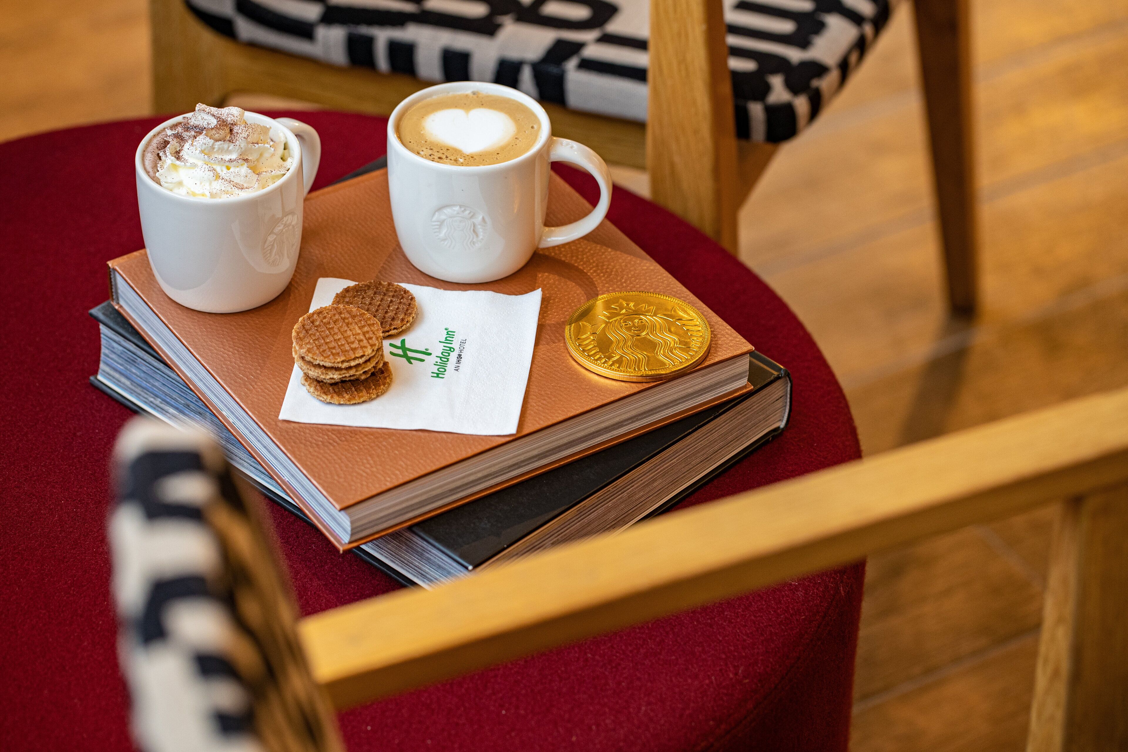 A table with two cups of coffee, a booklet, a coin, and a cookie.