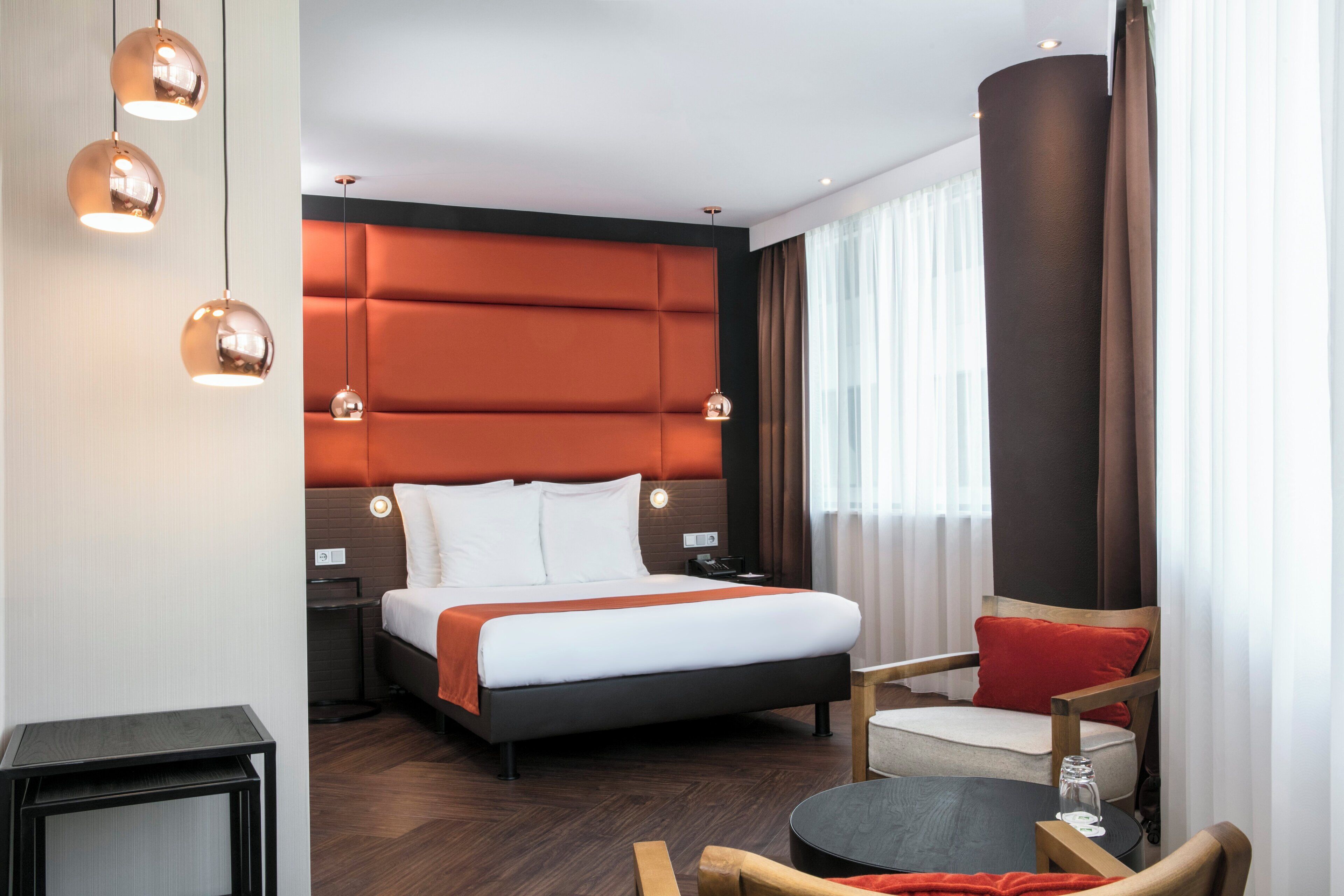 A hotel room with a bed, bedside tables, a chair, a small table, and a lamp.