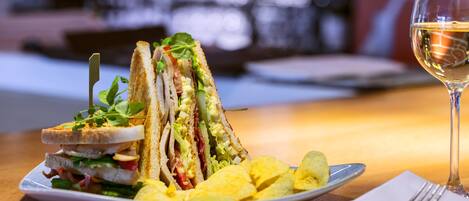 A sandwich with various fillings, a glass of white wine, and a plate of chips on a table.