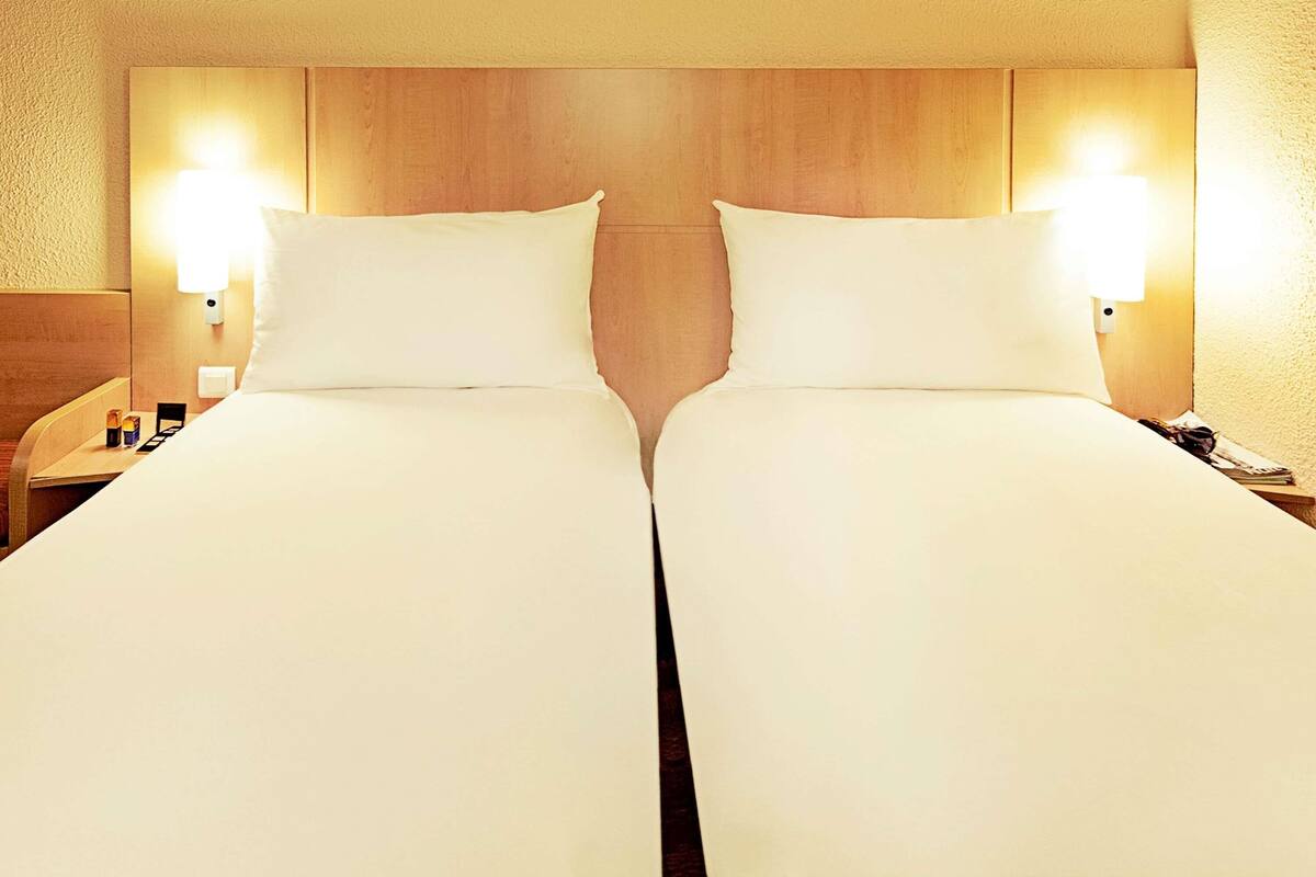 Une chambre d’hôtel avec deux lits, une tête de lit en bois, des lampes de chevet et une table de chevet avec un téléphone et une tasse.