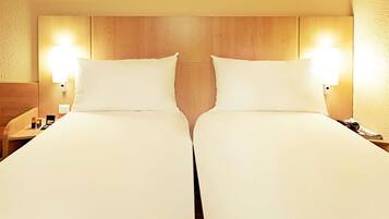 A hotel room with two beds, wooden headboard, bedside lamps, and a nightstand with a phone and a cup.