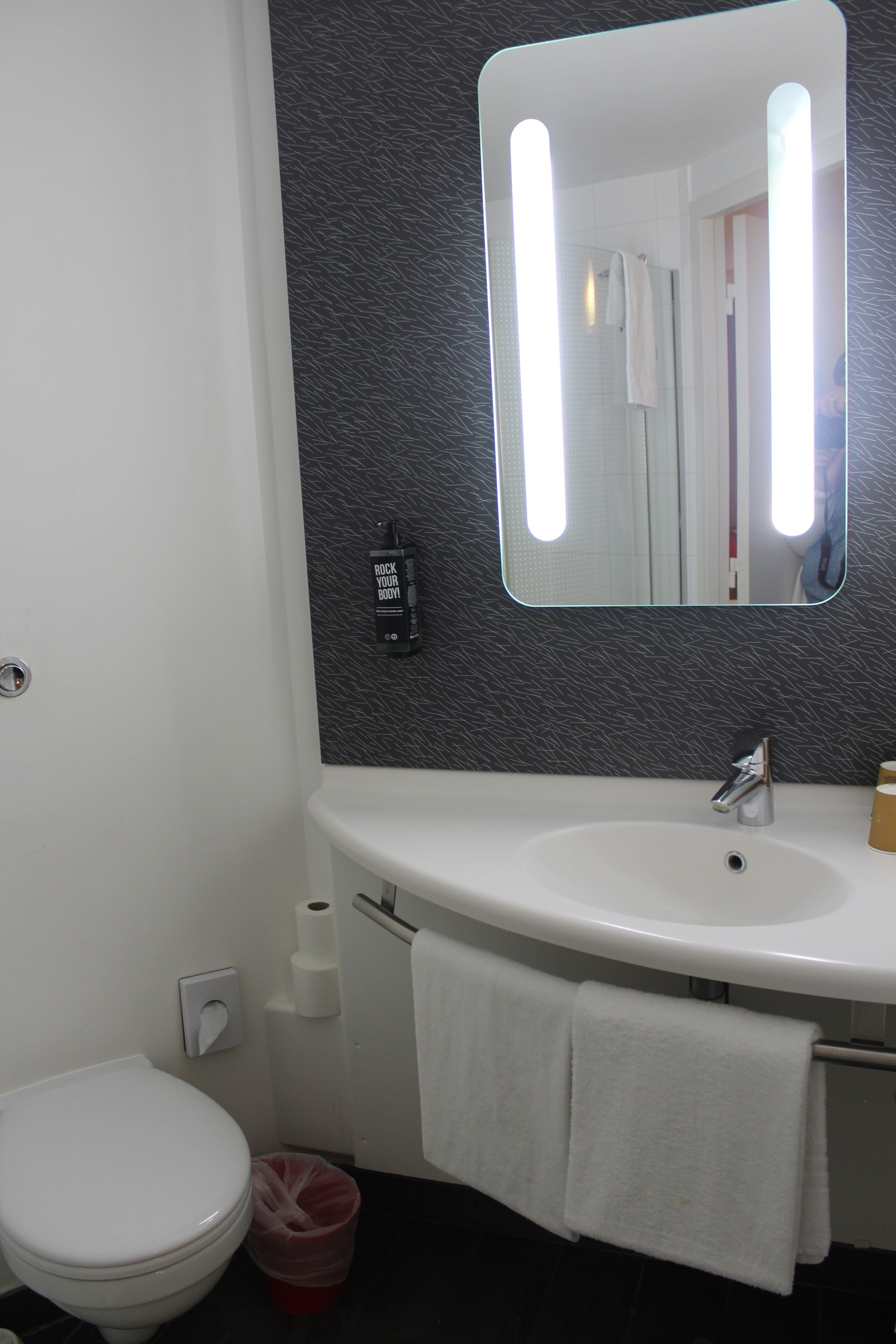A bathroom with a white toilet, a sink with a towel, and a mirror.