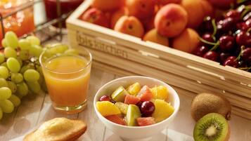 A breakfast setting with a bowl of mixed fruit, a glass of orange juice, and a variety of fresh fruits in a crate.