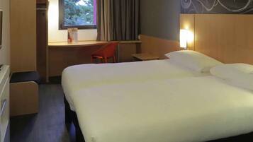 A hotel room with a double bed, a desk with a chair, a small table, and a window with curtains.