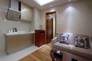 Una cocina moderna con horno integrado, un lavamanos y una encimera. Hay un armario de madera y una planta en la encimera. Un sofá color beige con cojines estampados se encuentra en la zona de estar.